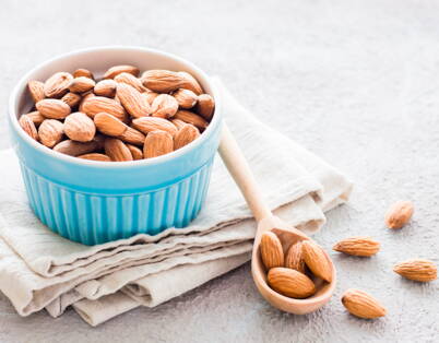 Mandorle in ciotola blu – snack sano Mandorle in ciotola blu con cucchiaio di legno – snack serale sano con acidi grassi preziosi