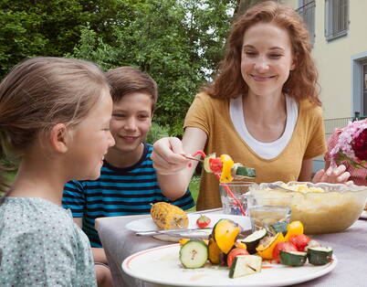 Familienessen im Garten Die Mutter reicht dein Kindern bunte Gemüsespiesse