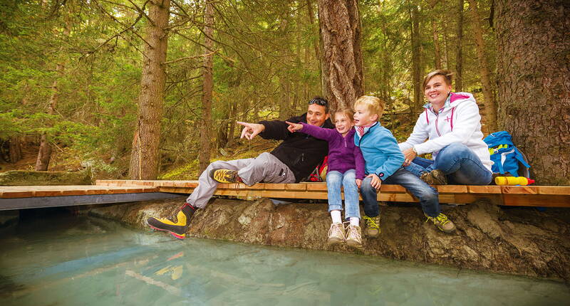 Familienausflug Rundweg Zauberwasser Grächen. Entdecke neue Orte der Ruhe und des Wohlfühlens und vitalisiere Geist und Seele. Entspanne dich an der «Genussinseln» bei einem Fussbad und erlebe ein unvergleichbares Sitz- und Liegegefühl.