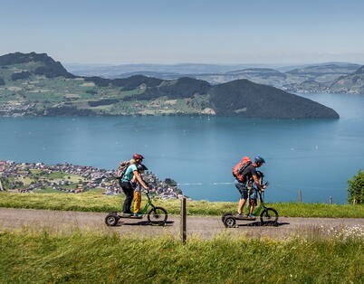 Drei Erwachsene auf dem Bikeboard flitzen ins Tal – mit der Gondelbahn im Hintergrund ein rasanter Familienspass in traumhafter Umgebung.