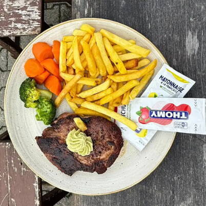 Teller mit Pommes, Steak und Kräuterbutter, Rüebli und Broccoli mit Mayonnaise und Ketchup auf einem verwitterten Holztisch am Alpen-Imbiss Leiterli