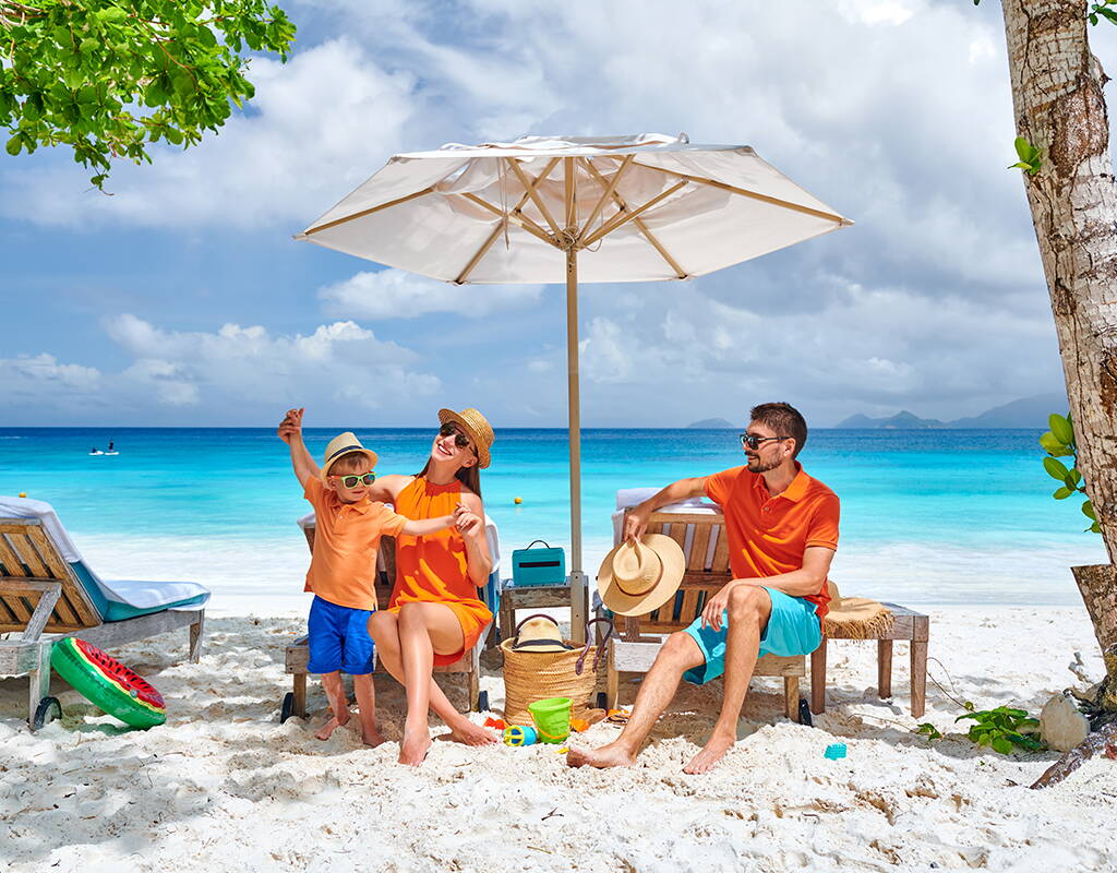 Scène de plage sous un parasol dans un cadre tropical. L’image suggère des vacances détendues et souligne l’importance d’une assurance voyage.