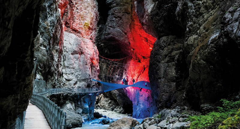 Section éclairée des gorges du glacier de Grindelwald avec une passerelle longeant des parois rocheuses imposantes.