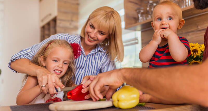 Un enfant coupe des légumes avec l’aide de sa mère dans la cuisine.
