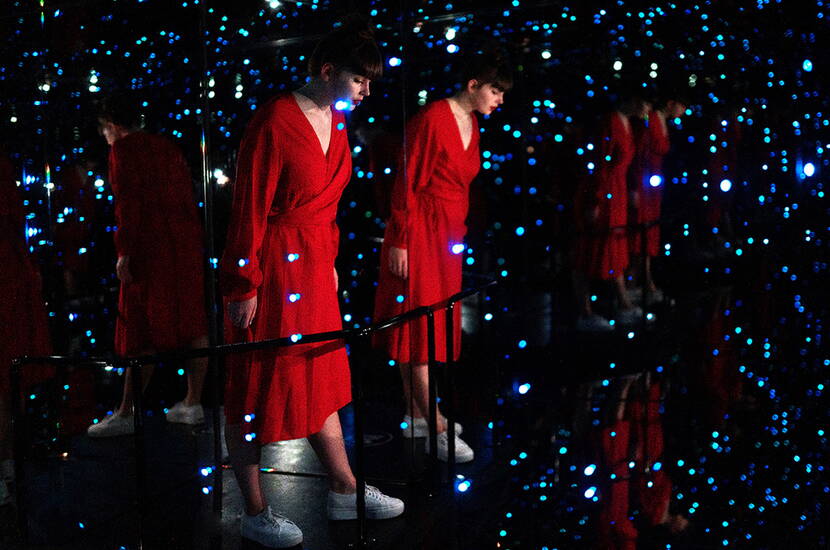 Person in rotem Kleid in einem Raum voller Spiegel und Lichter – eine endlose Illusion.