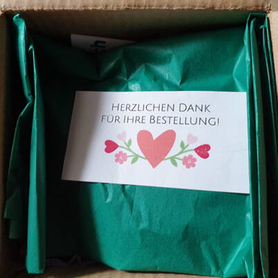 Ein geöffnetes Paket mit sorgfältig eingepacktem Cochenille‑Döschen und einem Dankeskärtchen – der Start für das natürliche Ostereierfärben.