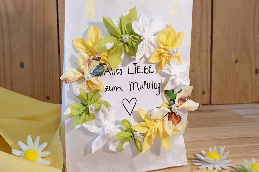 Für wenig Geld kannst du im Handumdrehen eine schöne Geschenktüte für den Muttertag basteln. Alles, was du dazu brauchst, ist eine Butterbrottüte, verschiedene Servietten, Dekomaterial und unsere Vorlagen mit Dankessprüchen zum kostenlosen Download.