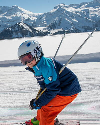 Un bambino scia con concentrazione su una pista appena preparata con uno splendido panorama alpino.