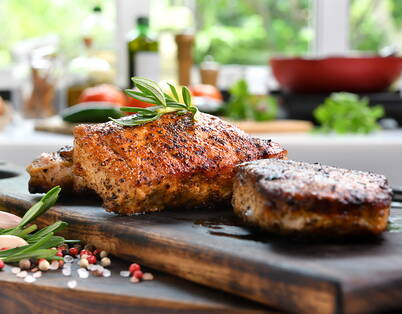 Pezzi di carne grigliati con rosmarino su tagliere di legno – la carne cotta si conserva 2-3 giorni in frigorifero e deve essere riscaldata ad almeno 70°C