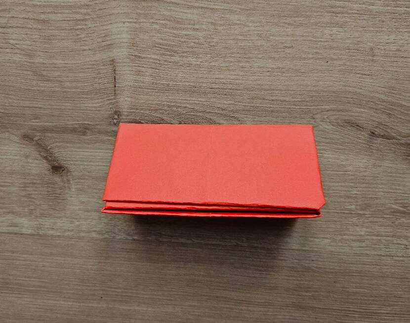 DIY Papierportemonnaie – Zusammengefaltete Mittelpartie Das Papier wurde längs zu einem kompakten Rechteck zusammengefaltet. In diesem Schritt entsteht die Mittelpartie des Papierportemonnaies, die später die Fächerstruktur bildet. Die sauberen Kanten sorgen für Stabilität und bereiten den abschliessenden Verschlussfalz vor.