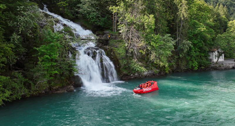 Das Jetboat hält vor den Giessbachfällen auf dem Brienzersee – spektakuläre Sicht auf Wasserfall, Wald und türkisgrünes Wasser.