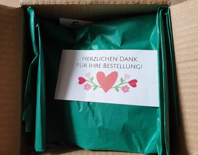 Un paquet ouvert contenant un petit pot de cochenille soigneusement emballé et une carte de remerciement – le début parfait pour une coloration naturelle des œufs.