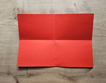 Papierportemonnaie falten – Grundfalten für die Orientierung Das rote Papier ist vollständig geöffnet und zeigt eine horizontale und vertikale Mittelfalte. Diese Grundfalten dienen als wichtige Orientierungslinien für den weiteren Faltprozess des DIY Papierportemonnaies und sorgen dafür, dass alle kommenden Schritte präzise und symmetrisch ausgeführt werden können.