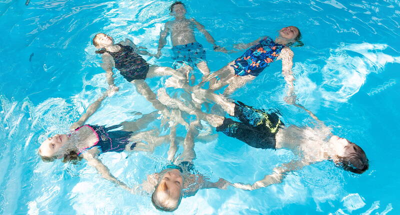 Un gruppo di bambini crea un cerchio galleggiante in piscina. Un esercizio giocoso che favorisce fiducia e coordinazione.