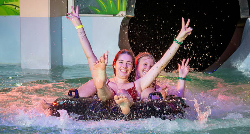 Due persone si tuffano in acqua da uno scivolo, con le braccia alzate e un sorriso sicuro. Emozioni forti garantite all’Aquaparc Le Bouveret!