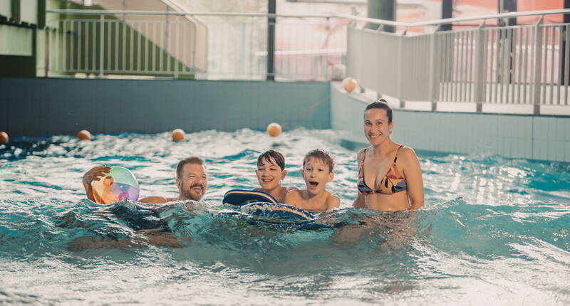 Personen geniessen das Wellenbecken mit Schwimmhilfen und Wasserball.