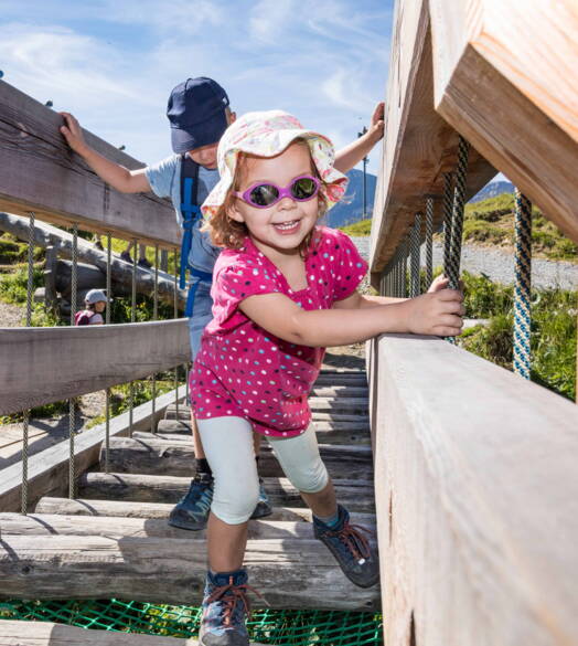 I bambini esplorano un parco giochi in legno sul Sentiero Marmotta nelle Alpi svizzere, un'attività all'aria aperta amata e conveniente per le famiglie, spesso gratuita o combinabile con sconti.
