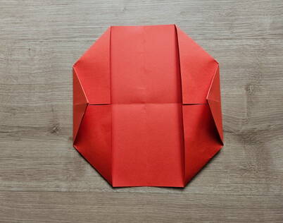 Origami Papierportemonnaie – Vier Ecken diagonal zur Mitte gefaltet Alle vier Ecken des roten Papiers wurden diagonal zur Mitte gefaltet und ergeben nun eine achteckige Form. Dieser Schritt bildet die stabile Grundstruktur des DIY Papierportemonnaies und sorgt dafür, dass die weiteren Faltungen sauber und symmetrisch bleiben. Die diagonalen Kanten geben dem späteren Portemonnaie seine charakteristische Form.