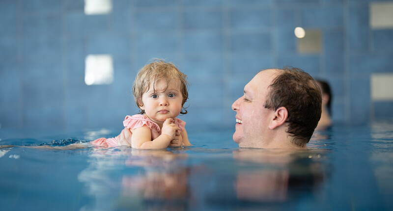 Un bambino vive un’esperienza serena e formativa in piscina, sostenuto da un adulto.