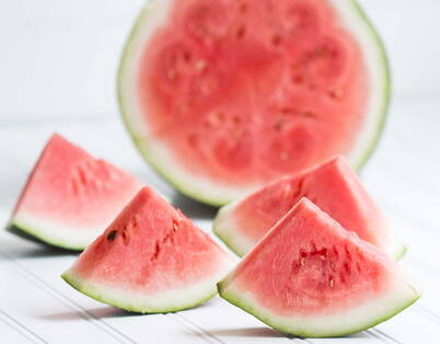 Geschnittene Wassermelone Eine halbierte Wassermelone mit vier geviertelten Melonenstücken.