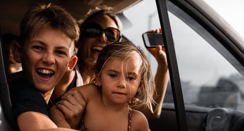 Familie mit Kindern sitzt im Auto im Stau vor dem Gotthard-Tunnel und überbrückt die Wartezeit gemeinsam auf der Ferienreise.