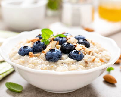 Porridge mit frischen Blaubeeren und Mandeln Cremiger Haferbrei, garniert mit saftigen Blaubeeren, gehackten Mandeln und einem frischen Minzblatt – ein nährstoffreiches Frühstück voller Geschmack.