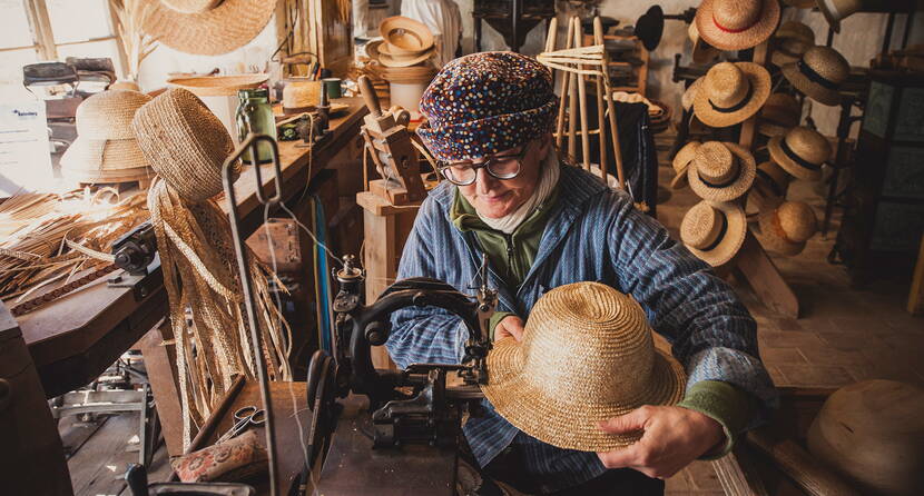 Die Handwerkerin über näht die Krempe eines Strohhuts