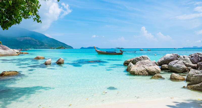 Weisser Sandstrand, ruhiges Wasser und traditionelle Boote vor grünen Hügeln.