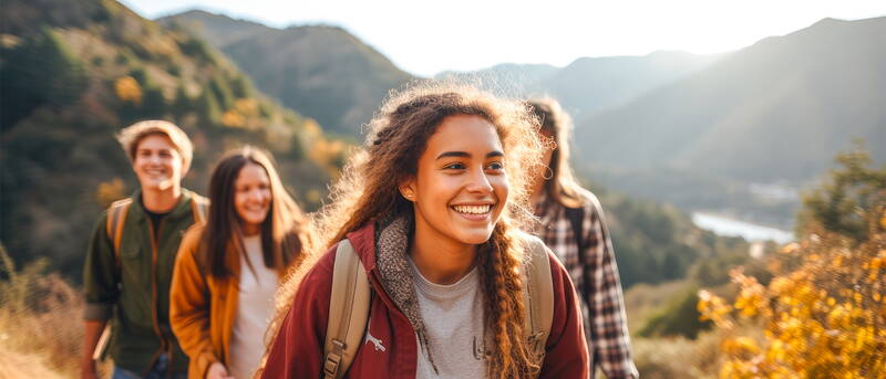 Un groupe de jeunes avance sur un sentier de montagne, entouré de couleurs d’automne et d’une lumière douce.